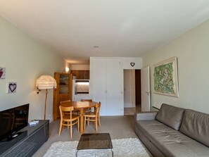 A living room with a sofa, a coffee table, a TV, a dining table with chairs, a kitchen area with cabinets, and a door leading to another room. - Bright apartment at the foot of the slopes with free WIFI (Flaine)