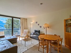 A modern living room with a sofa, a dining table with chairs, a TV, and a view of the outdoors. - Bright apartment at the foot of the slopes with free WIFI (Flaine)