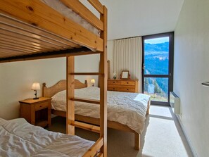 A bedroom with bunk beds, a dresser, a nightstand, and a window with a mountain view. - Bright apartment at the foot of the slopes with free WIFI (Flaine)