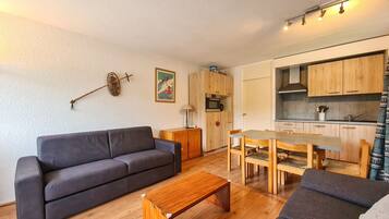 Un espace de vie compact comprenant un canapé, une table basse, une table à manger avec des chaises, un coin cuisine et un petit meuble de rangement.