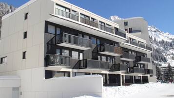 Un hôtel à plusieurs étages, doté de balcons, de grandes fenêtres et surplombant un paysage montagneux enneigé.