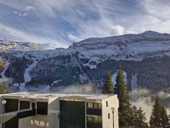 Um edifício moderno com telhado plano, rodeado por montanhas cobertas de neve e pinheiros.