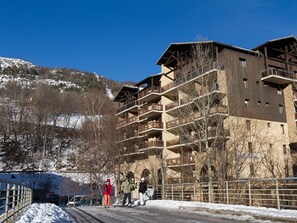 A multi-story building with balconies, a ski slope in the background, and a clear sky.