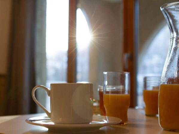 A table with a white cup and saucer, a glass of orange juice, and a pitcher of orange juice.