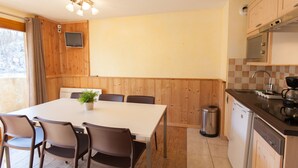 Una cocina compacta con armarios de madera, una mesa de comedor con sillas, un pequeño cubo de basura y un horno empotrado.