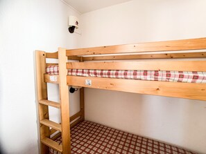 Uma cama beliche com colchão xadrez, uma escada e um ponto de luz fixado na parede.