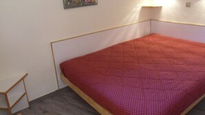 Ein kleines Zimmer mit einem Einzelbett, einem Holzkopfende, einem an der Wand befestigten Bilderrahmen und einer Nachttischlampe.