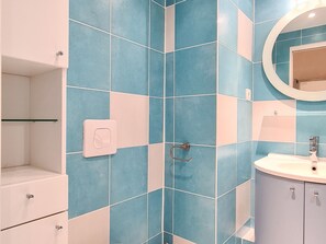 Une salle de bain avec des carreaux bleus et blancs, un distributeur de serviettes blanc, un porte-serviettes et un miroir rond au-dessus d’un lavabo.