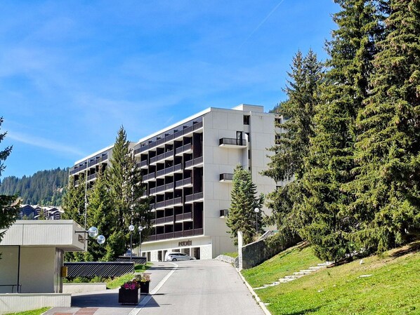 A multi-story building with a modern architectural style, featuring balconies and a parking area in front.