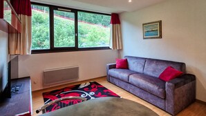 A room with a grey sofa, red cushions, a window with curtains, a radiator, and a painting on the wall. - Renovated studio for 4, near slopes in Flaine (Flaine)
