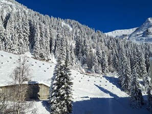 A snow-covered mountain landscape with a ski slope, a wooden building, and evergreen trees.
