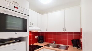 Una cocina compacta con armarios blancos, un backsplash de azulejos rojos, horno integrado, cafetera y lavavajillas.
