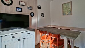 Una cocina moderna con televisor integrado, armarios de madera y un comedor con mesa de madera y sillas naranjas.