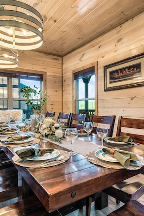 A wooden dining room with a long table set for a meal, featuring woven placemats, plates, and glassware. - Hummingbird Hill Vista- Pool HotTub View (Pigeon Forge)