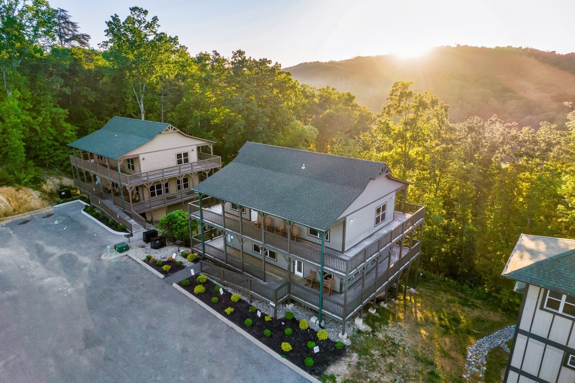 A two-story lodge with a balcony and a covered patio area, surrounded by dense forest and hills.