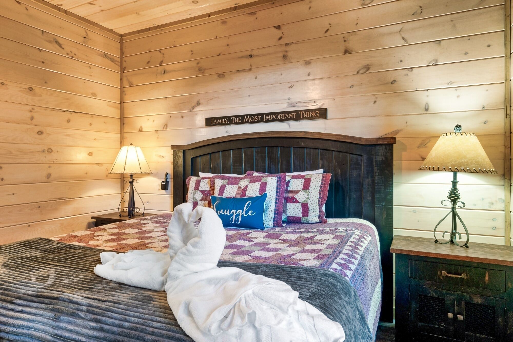 A cozy wooden room with a bed, a sign above the bed reading "FAMILY. THE MOST IMPORTANT THING", and a lamp on the nightstand.