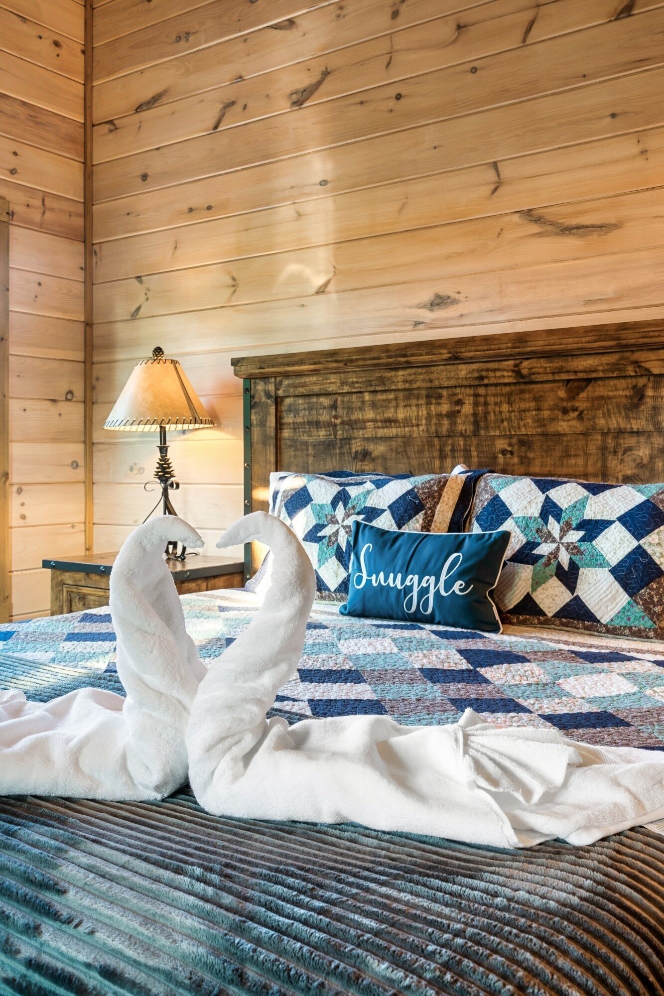 Une pièce chaleureuse avec un plafond en bois, un lit recouvert d’une couette bleue et blanche, et un oreiller orné du mot « Suggelle ».