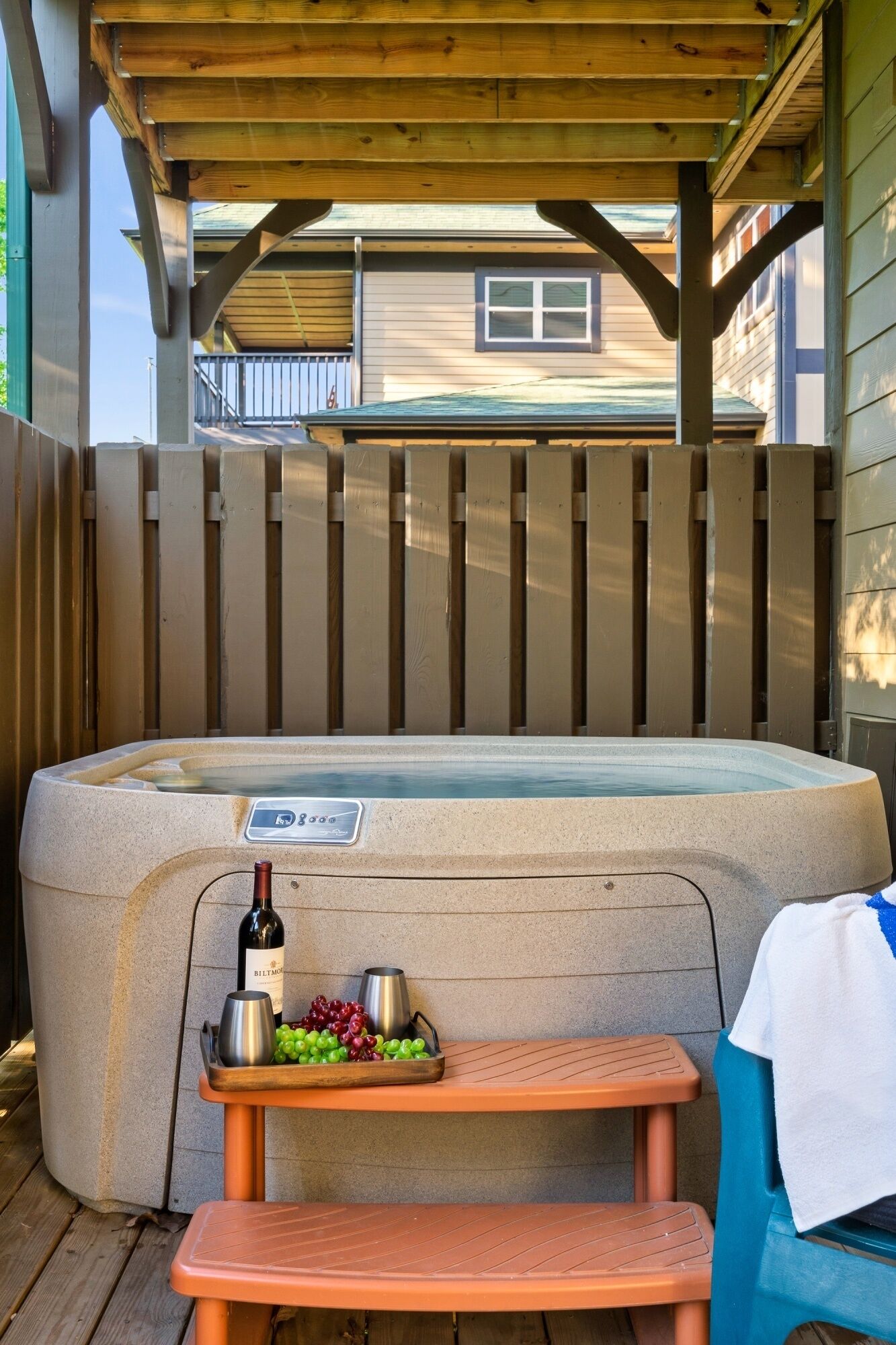 A hot tub with a control panel, a bottle of wine, and a tray with grapes and a thermos.