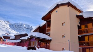A snow-covered building with multiple balconies and a mountainous backdrop.