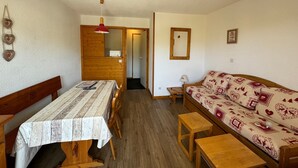 A cozy room with a wooden dining table, benches, a patterned sofa, and a small wooden stool.