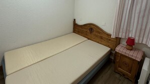 A small, single-bed room with a wooden headboard, a small wooden cabinet with a red lamp, and a striped curtain.