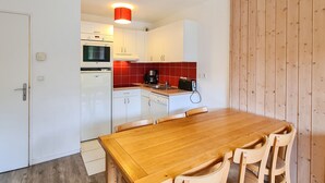 Eine kleine Küche mit weißen Schränken, einer roten gefliesten Spritzschutzwand, einem Holztisch und Holzvertäfelung.