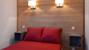 Een slaapkamer met een houten hoofdbord, twee nachtkastjes, een bed met rode beddengoed en wandlampen.