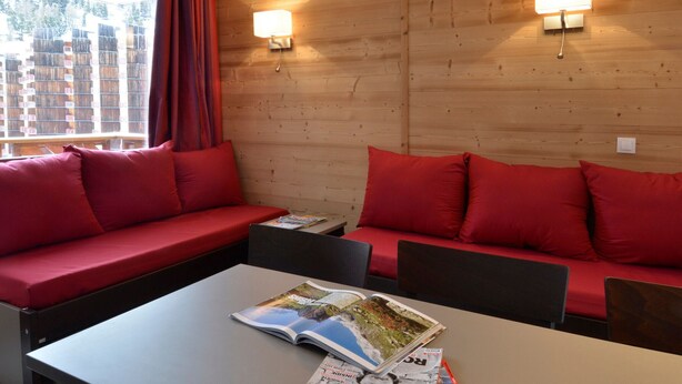 Een kamer met een houten wand, twee rode banken, een tafel met tijdschriften en twee wandlampen.