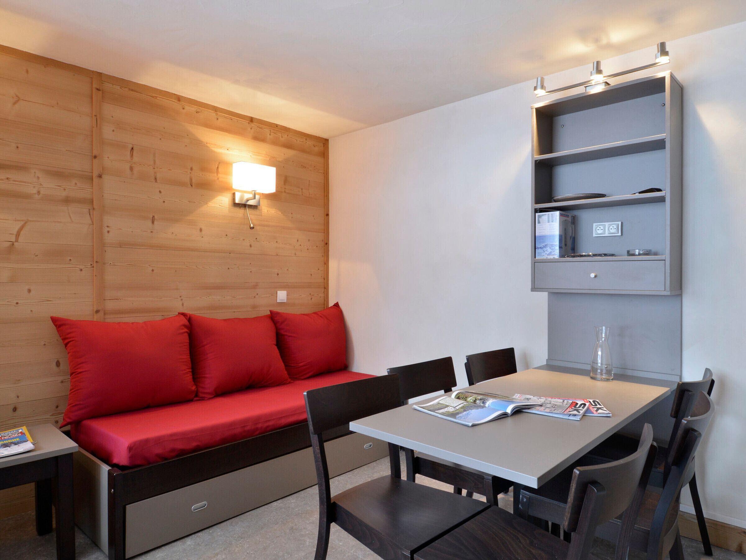 Ein modernes Zimmer mit einer Holzwand, einem roten Sofa, einem Esstisch mit Stühlen und einer eingebauten Vitrine mit einer Lampe.