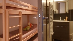 Ein Stockbett mit einer Leiter, ein Stofftier und eine Tür zu einem Badezimmer mit Spiegel und Waschbecken.