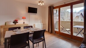Ein Essbereich mit Tisch für vier Personen, einem an der Wand montierten Fernseher und einer Glastür zu einem Balkon.
