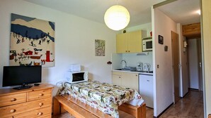 A compact bedroom with a wooden bed, a TV on a dresser, a microwave, and a kitchenette with a sink and cabinets. - Comfortable studio with balcony in Flaine center (Flaine)