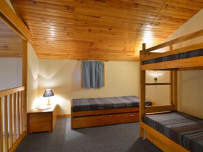 A bunk bed room with a wooden ceiling, a desk with a lamp, and a window with a curtain.