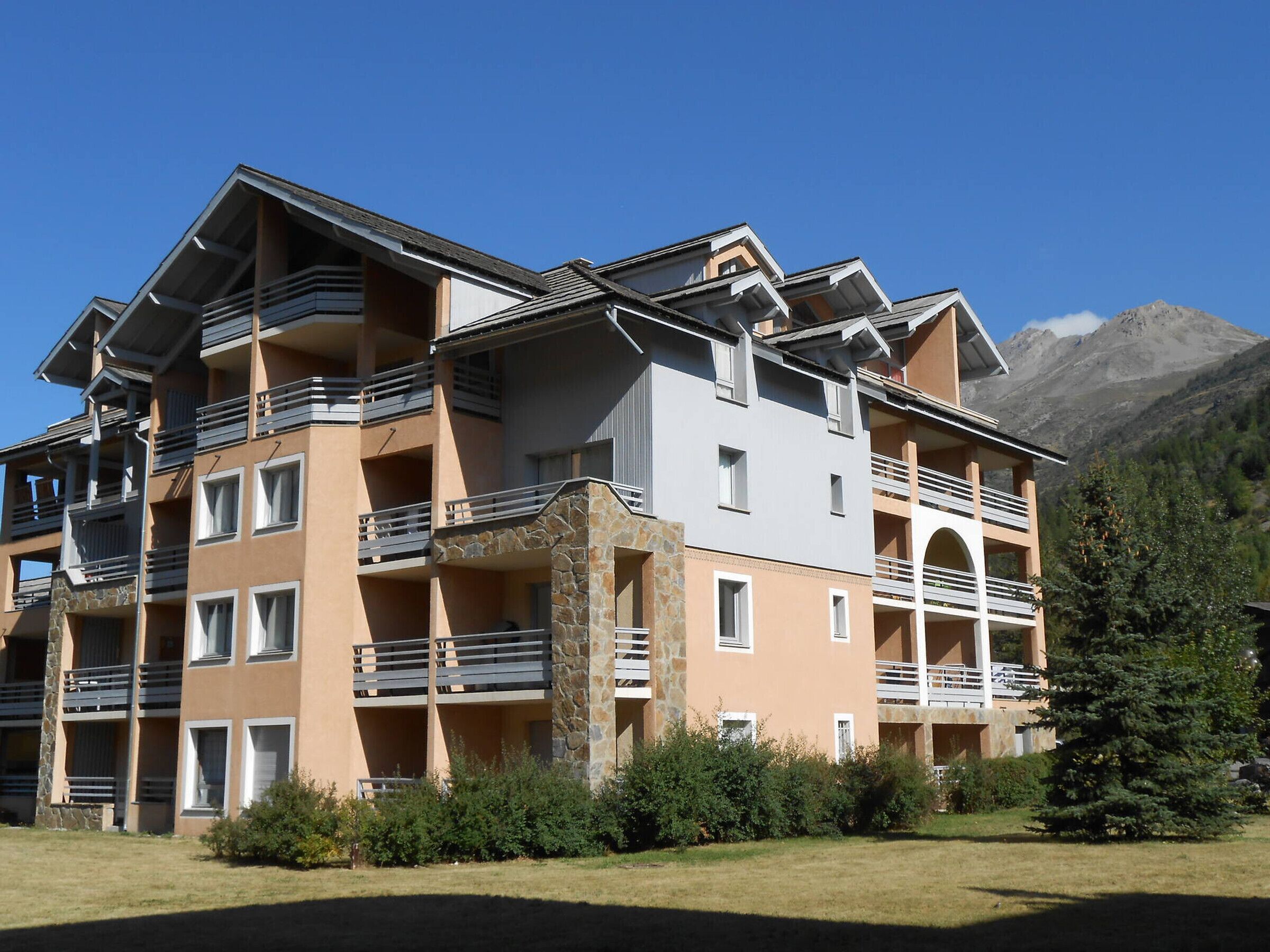 A multi-story hotel with balconies, stone pillars, and a mountainous backdrop.