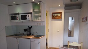 Et kompakt køkken med mikrobølgeovn, kaffemaskine og vask. Der er et lille spiseområde med et bord og stole.