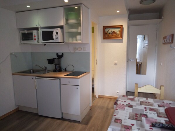 A compact kitchen with a microwave, coffee maker, and a sink. There's a small dining area with a table and chairs.