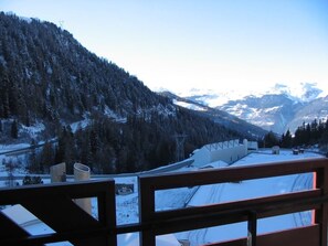 A view from a window overlooking a snowy mountain landscape with a wooden railing.