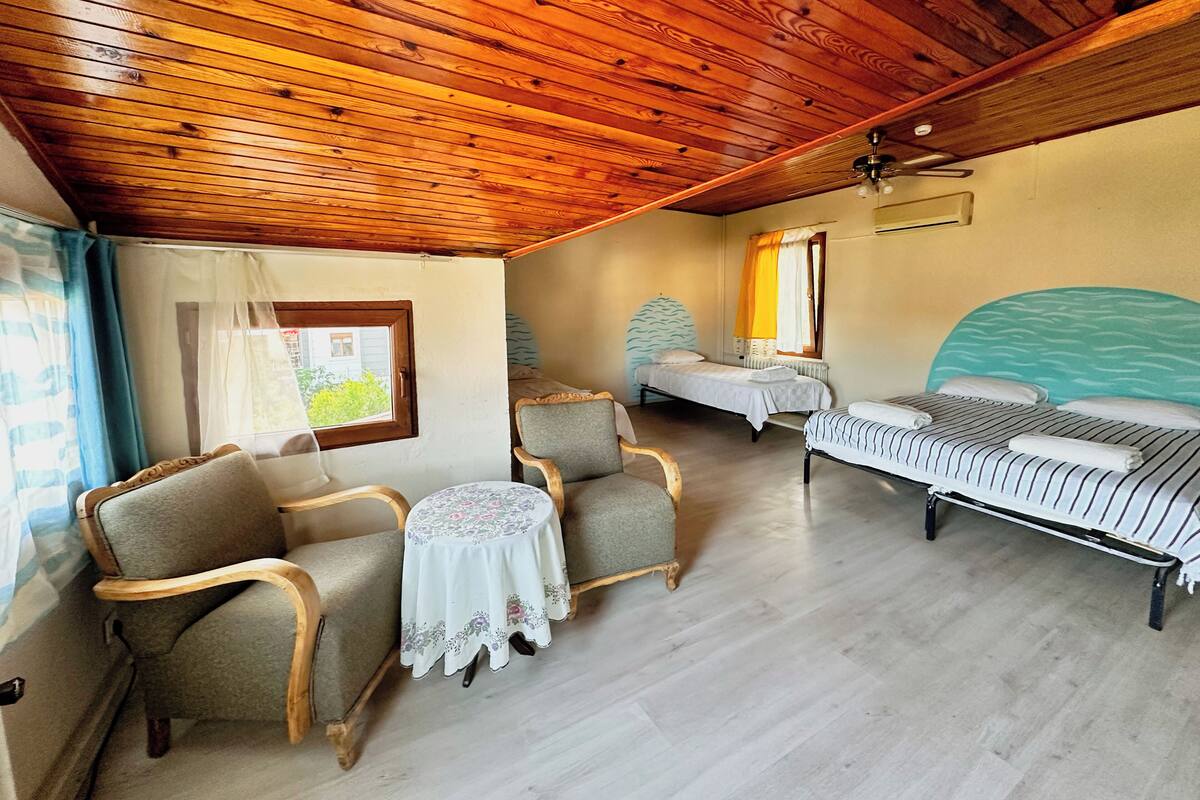 Una habitación con dos camas, techo de madera, una mesita con mantel floral y una silla.