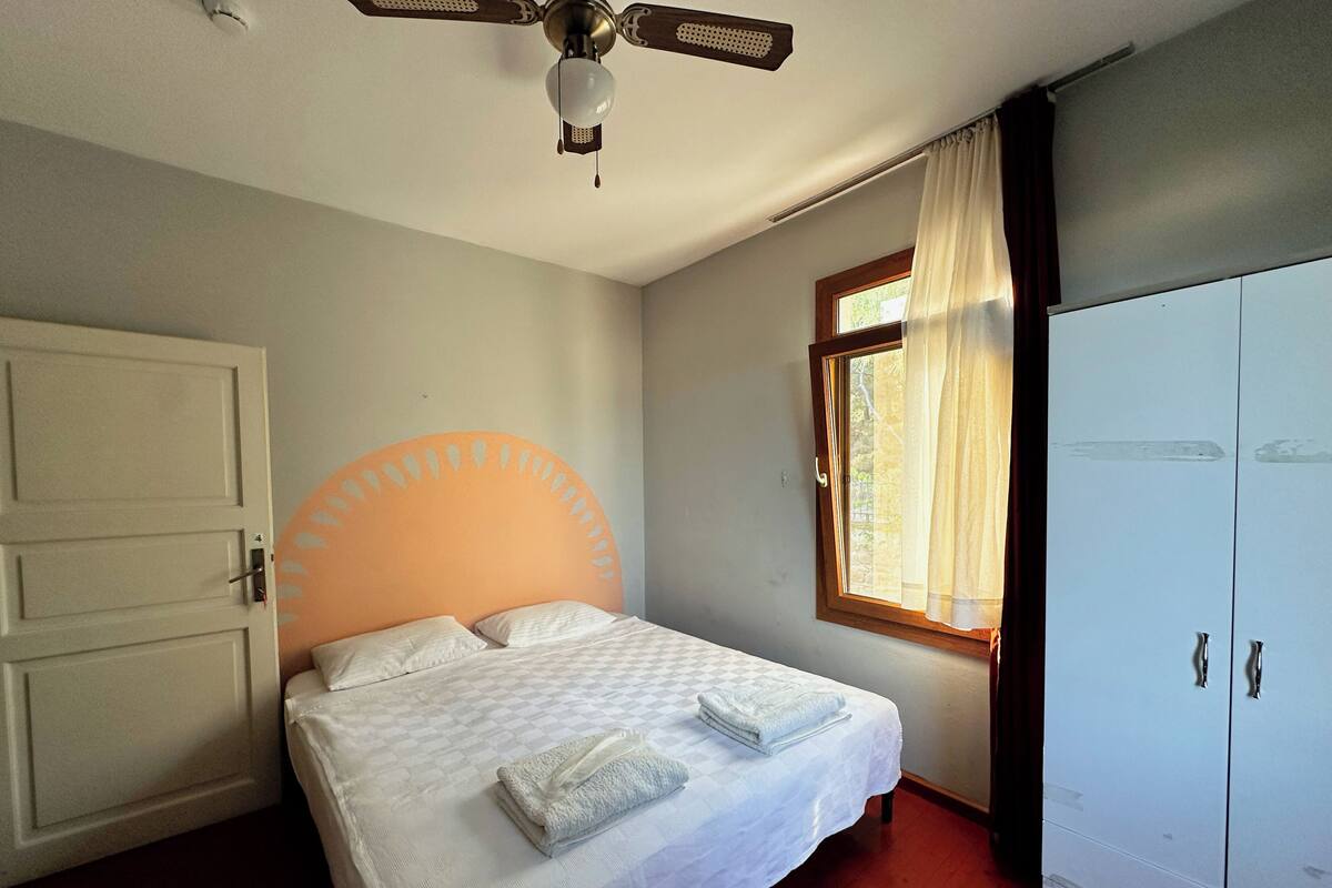 Un dormitorio con cama, armario, ventana con cortinas y ventilador de techo.