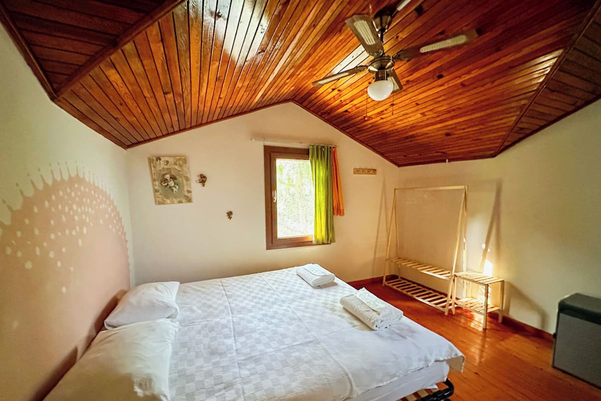 Un dormitorio con techo de madera, una cama con ropa de cama blanca, una ventana con cortinas y un ventilador de techo.