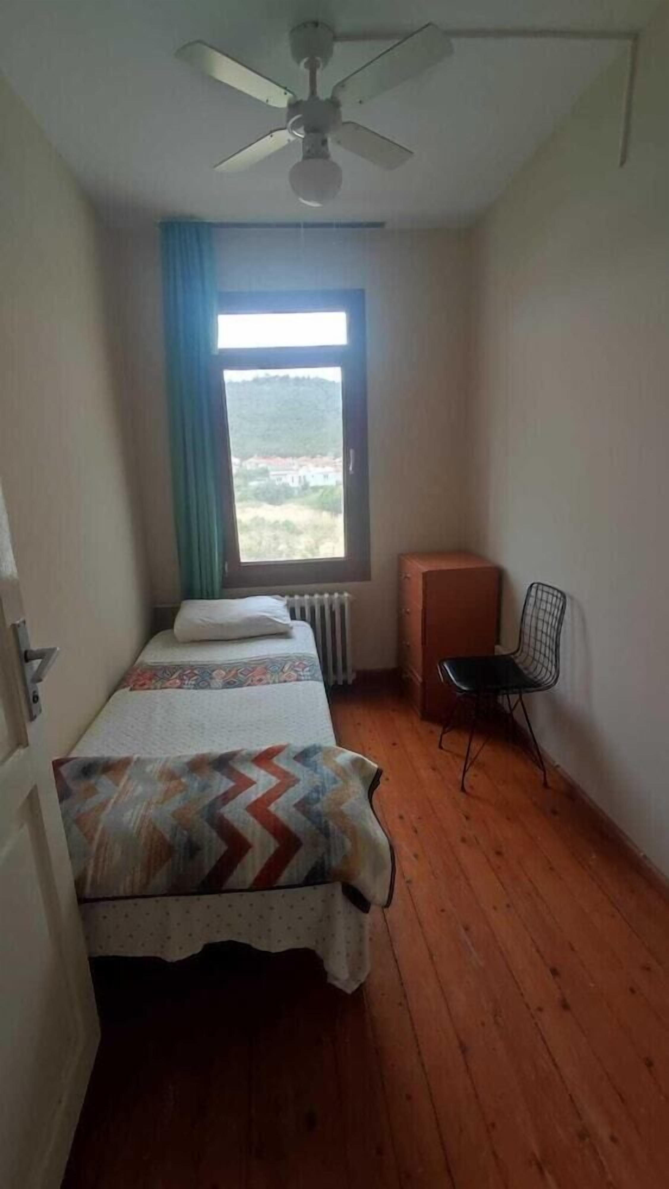Ein Zimmer mit einem Bett, einem Sessel, einem Fenster mit Blick und einem Deckenventilator.