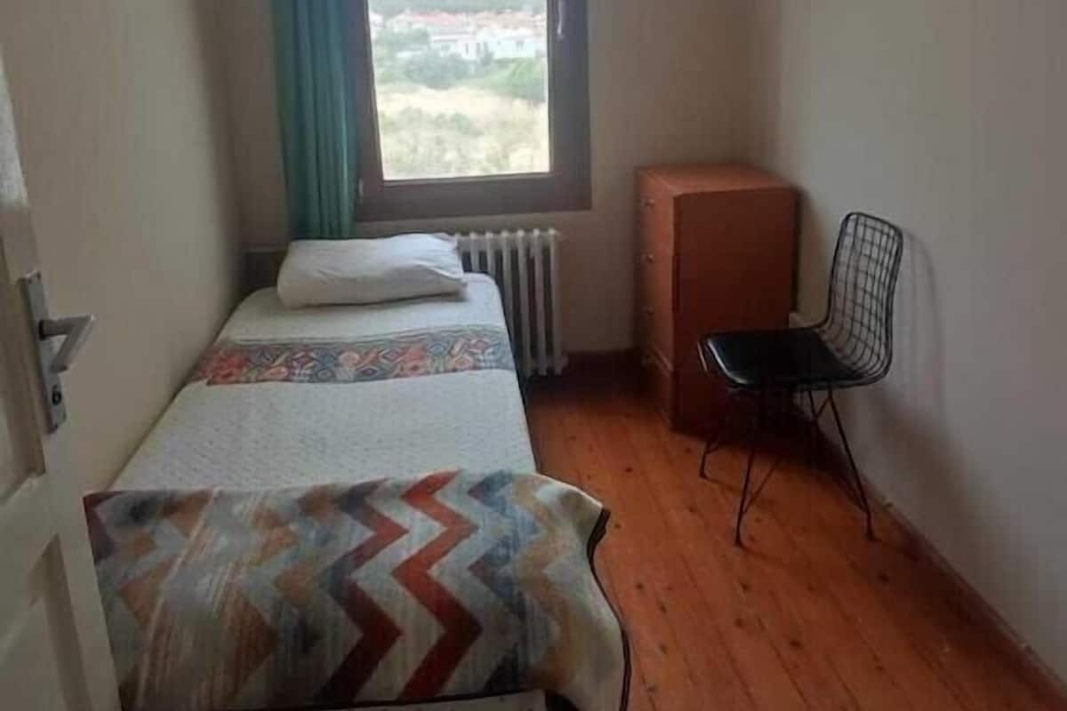 Una habitación con una cama, una silla, un ventanal con vistas y un ventilador de techo.