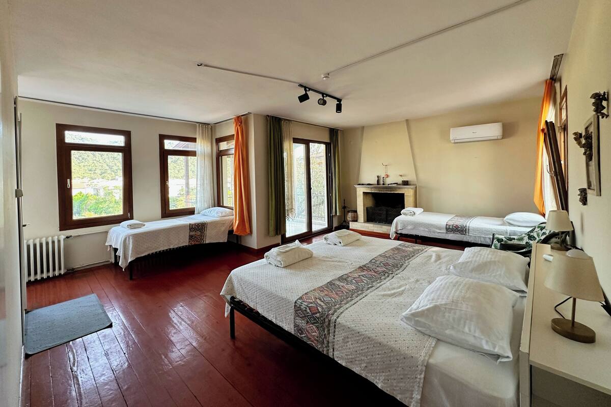 Habitación de hotel con dos camas individuales, chimenea y ventanas amplias con cortinas.