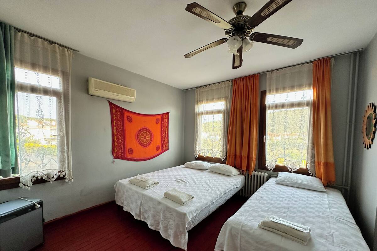 Una habitación de hotel con dos camas, un ventilador de techo y una ventana con cortinas.