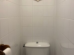 Une salle de bain avec des murs recouverts de carreaux blancs et des toilettes blanches.