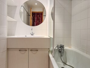 Une salle de bain avec un lavabo blanc, un miroir et une baignoire.