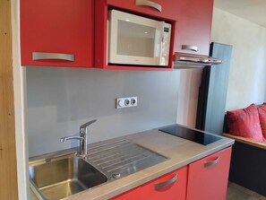 Cocina compacta con pileta de acero inoxidable, microondas y alacenas rojas.