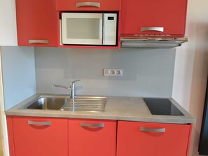 Una cocina pequeña con microondas, lavamanos y armarios rojos.