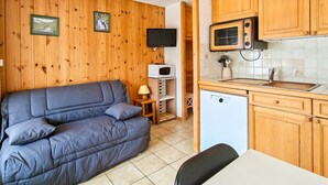 Ett kompakt bostadsutrymme med en soffa, ett litet kök, träväggar och en tv.