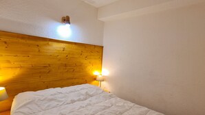 Ett sovrum med en sänggavel i trä, ett vitt sängöverkast och två sänglampor.